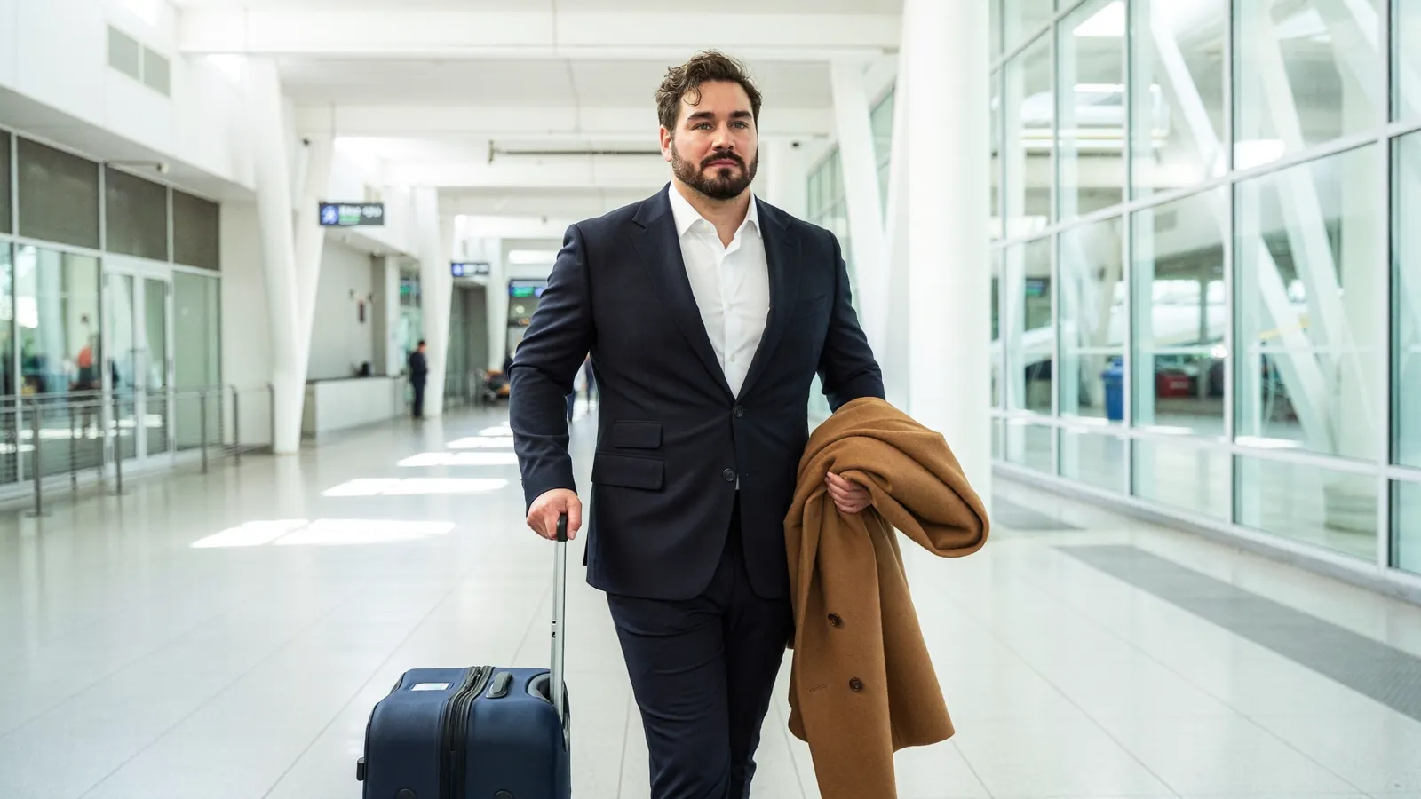 Ivo Schönberner geht mit Rollkoffer und Mantel durch ein helles Flughafenterminal
