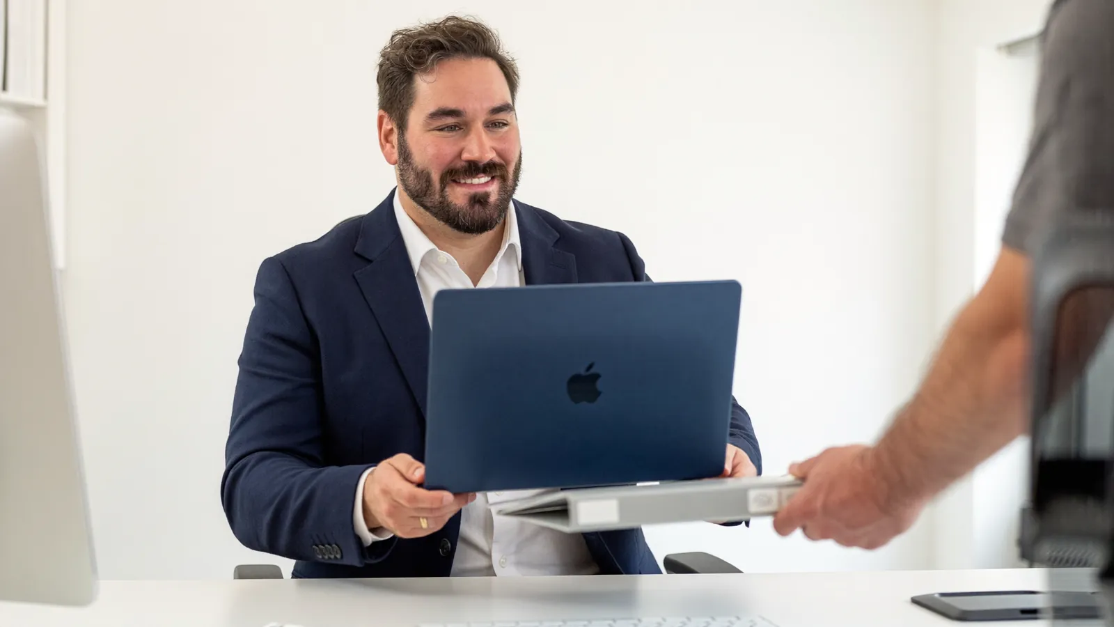 Ivo Schönberner übergibt einem Nachfolger ein MacBook und eine Dokumentationsmappe